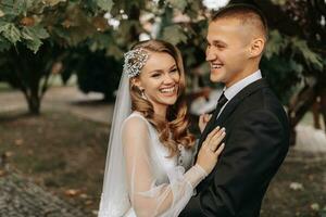 coppia nel amore nel il autunno parco. bionda sposa nel un' nozze vestito con maniche. sposo nel un' classico nero completo da uomo, bianca camicia e legare. sorrisi e gioia foto