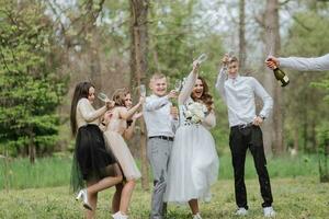 il sposa e sposo e loro amici posa contro il sfondo di il foresta. un' grande gruppo di persone siamo avendo divertimento a loro gli amici' nozze. Champagne spruzzi ovunque foto