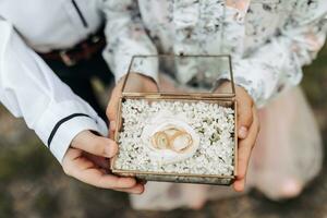 nozze anelli di il sposa e sposo nel un' bicchiere scatola su un' peonia fiore. figli di mani hold nozze anelli. avvicinamento foto