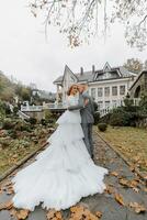 un' camminare di il sposa e sposo nel un' parco con bellissimo architettura, bianca ringhiere. sposa con un' lungo treno foto
