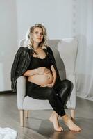 elegante studio ritratto di un' bellissimo incinta giovane donna su un' sedia nel un' nero completo da uomo foto