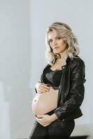 elegante studio ritratto di un' bellissimo incinta giovane donna nel un' nero completo da uomo foto