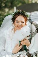 giovane elegante sposa nel un' bianca vestito con un' tiara di fresco fiori su sua testa in posa nel il giardino con sua barboncino cane foto