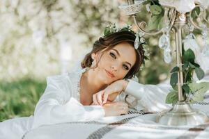 ritratto di il sposa nel il giardino. il bellissimo sposa è indossare un' bianca vestito e un' tiara di fresco fiori su sua testa foto