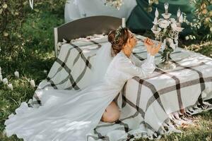 mattina di il sposa a il letto nel il giardino. il bellissimo sposa è indossare un' bianca vestito e un' tiara di fresco fiori su sua testa foto