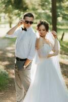 alla moda sposo e carino sposa nel bianca vestito con tiara di fresco fiori, abbracciare, ridendo nel parco, giardino, foresta all'aperto. nozze fotografia, ritratto di sorridente Novelli sposi. foto