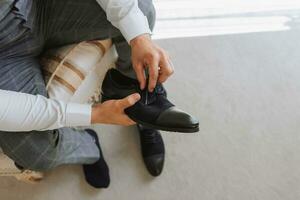 un' elegante sposo è preparazione per il nozze cerimonia. quello dello sposo mattina. il uomo d'affari indossa nero scarpe. il sposo è ottenere pronto nel il mattina prima il nozze cerimonia foto