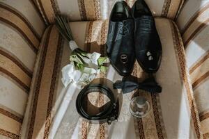 dettagli di il sposo su il sedia. nero velluto stivali, oro nozze anelli, Uomini profumo, gemelli, un' mazzo di calla fiori foto