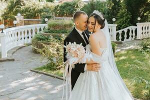 ritratto di un' giovane bellissimo nozze coppia nel il giardino, il sposa nel un fuori dalla spalla nozze vestire, il sposo nel un' nero classico completo da uomo foto