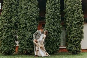 sposo e sposa nel il parco nel natura, verde thuja alberi su il sfondo. bacio. foto ritratto. nozze coppia