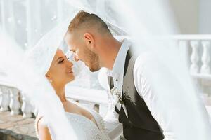 un' elegante coppia di europeo Novelli sposi. sorridente sposa nel un' bianca vestire. il sposo, vestito nel un' classico nero completo da uomo, bianca camicia, sotto un' velo. nozze nel natura foto