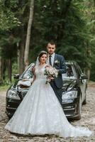 davanti Visualizza di un' sposato sposa e sposo indossare festivo Abiti in piedi contro un' nero auto su loro nozze giorno foto