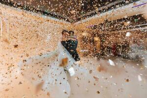 bellissima sposa e elegante sposo danza sotto d'oro coriandoli a nozze ricezione. contento nozze coppia l'esecuzione primo danza nel ristorante. romantico momenti foto