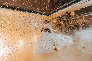 bellissima sposa e elegante sposo danza sotto d'oro coriandoli a nozze ricezione. contento nozze coppia l'esecuzione primo danza nel ristorante. romantico momenti foto