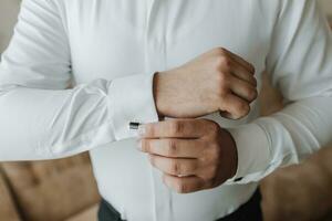 il uomo si allaccia il pulsanti su il suo camicia manica. il sposo è preparazione per il nozze. foto