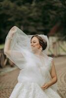 nozze ritratto. il sposa nel un' bianca vestito su il ponte con un' svolazzanti velo. sincero Sorridi. vento e velo. diadema. foto