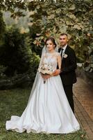 alla moda sposo e carino brunetta sposa nel bianca vestito con professionale trucco e mazzo di fiori siamo abbracciare, ridendo nel parco, giardino, foresta all'aperto. nozze fotografia foto