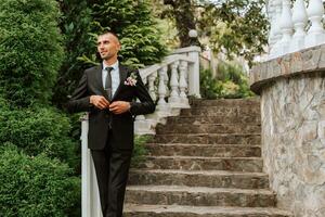 un' uomo nel un' classico nero completo da uomo e bianca camicia sta e pose vicino il pietra passi. un' elegante guarda. Uomini stile. moda. attività commerciale. foto