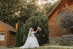 un' elegante sposo nel un' nero completo da uomo e un' carino sposa nel un' bianca vestito con un' lungo velo siamo abbracciare e a piedi vicino verde alto alberi. nozze ritratto di sorridente e contento Novelli sposi. foto