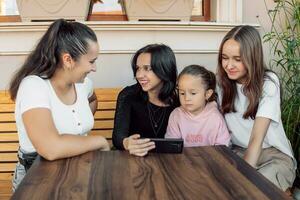 adolescenti e uno bambino avendo divertimento all'aperto nel un' bar. amicizia di bambini e adolescenti. quattro ragazze, vestito nel diverso Abiti, grido su il Telefono foto