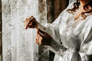 bellissimo sposa nel un' bianca accappatoio nel il mattina. il sposa è preparazione per il nozze. professionale trucco e capelli. un' corona su il testa e un' lungo velo di il sposa foto