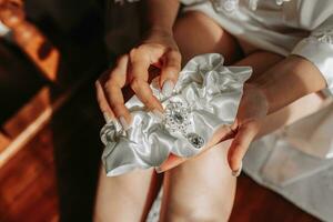 il sposa nel un' bianca accappatoio detiene un' giarrettiera nel sua mani. tenero mattina di il sposa. foto