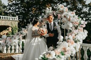 contento sposa e sposo siamo in posa a il nozze cerimonia. il nozze arco è decorato con rosa fiori foto