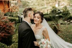 bellissima elegante lussuoso sposa con velo soffiaggio nel il vento. e un' elegante sposo bacio all'aperto vicino alto autunno alberi foto