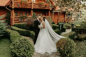 bellissima elegante lussuoso sposa con velo soffiaggio nel il vento. e un' elegante sposo bacio all'aperto vicino alto autunno alberi foto