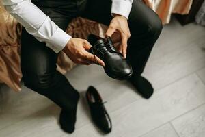 un' uomo nel un' bianca camicia, allacciatura nero scarpe e preparazione per incontrare il suo sposa. il uomo indossa classico nero scarpe foto