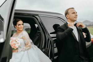 elegante nozze coppia, sposa, sposo in posa vicino il auto nel autunno. contento romantico giovane coppia festeggiare loro matrimonio. aprire. un' tenero momento. sposa con un' mazzo di fiori foto