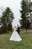 contento elegante coppia di Novelli sposi nel il verde foresta su un autunno giorno. il sposa nel un' classico lungo bianca vestito e il sposo nel un' blu completo da uomo abbraccio. nozze giorno. foto