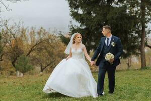 contento elegante coppia di Novelli sposi nel il verde foresta su un autunno giorno. il sposa nel un' classico lungo bianca vestito e il sposo nel un' blu completo da uomo abbraccio. nozze giorno. foto