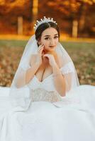 un' bellissimo sposa è seduta su il erba vicino il autunno le foglie di il alberi. nozze ritratto di un' giovane sposa nel un autunno tema. nozze fotografia. foto