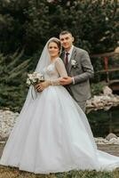 elegante sposa e sposo teneramente abbraccio e bacio. bellissimo sposa con moderno mazzo Abbracciare una persona elegante sposo nel autunno parco. sensuale romantico momento. nozze. elegante e Bellissima. foto