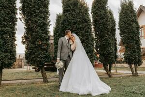 elegante sposa e sposo teneramente abbraccio e bacio. bellissimo sposa con moderno mazzo Abbracciare una persona elegante sposo nel autunno parco. sensuale romantico momento. nozze. elegante e Bellissima. foto