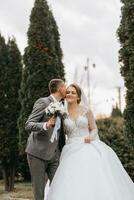 elegante sposa e sposo teneramente abbraccio e bacio. bellissimo sposa con moderno mazzo Abbracciare una persona elegante sposo nel autunno parco. sensuale romantico momento. nozze. elegante e Bellissima. foto