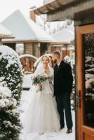 bellissimo e contento sposa e sposo siamo avendo divertimento tra nevoso alberi. sposa e sposo nel il inverno parco. sposa con un' mazzo di fiori nel un' nozze vestito e poncho. sposo nel un' nero cappotto. foto