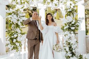 sensibile cerimonia di il sposa e sposo. un' contento sposini coppia sta contro il sfondo di un' nozze arco decorato con fresco fiori. il sposa e sposo mostrare via loro nozze anelli foto