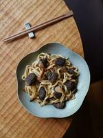 udon tagliatelle con funghi nel un' piatto su un' di legno tavolo. foto