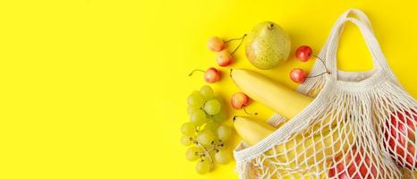 frutti maturi in borsa a rete su sfondo giallo. borsa a tracolla in cotone ecologico per lo shopping. alimenti vegani dietetici biologici. formato striscione. foto