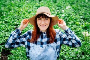 Ritratto donna agricoltore sorridente in telecamera che indossa un cappello di paglia nel suo orto foto