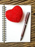 vista dall'alto di taccuino e penna con cuore rosso su sfondo nero in legno, san valentino foto