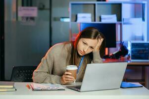 attività commerciale donna potabile caffè per ottenere alcuni energia per Lavorando col tempo seduta a scrivania utilizzando computer e fare col tempo foto