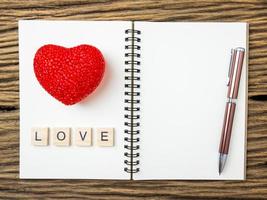 vista dall'alto di taccuino e penna con cuore rosso su sfondo nero in legno, parola d'amore in cubo di legno, san valentino foto