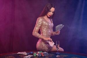 ragazza giocando poker a casinò, Tenere i soldi, carte. seduta su tavolo con patatine fritte, Champagne, denaro contante su esso. Nero, Fumo sfondo. avvicinamento. foto