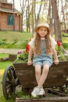 sognante preteen ragazza seduta su Vintage ▾ di legno carrello decorato come fiore letto a nazione tenuta foto