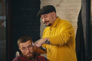 barbiere che fa taglio di capelli di attraente uomo barbuto nel negozio di barbiere foto