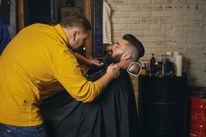 cliente con grande nero barba durante barba rasatura nel barbiere negozio foto