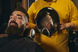 cliente con grande nero barba durante barba rasatura nel barbiere negozio foto